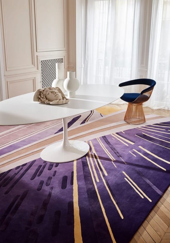 Modern dining room with a white table, artistic decor, and a purple geometric rug with yellow accents.