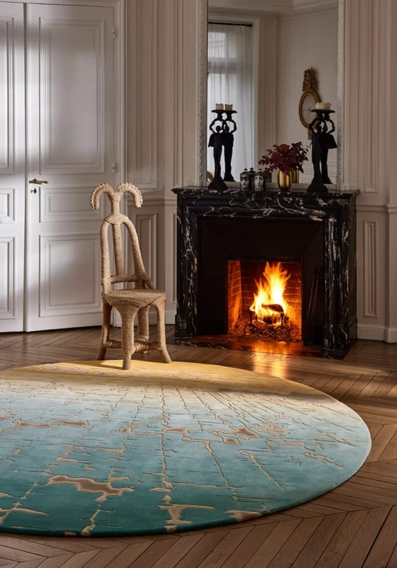 Elegant room with a round rug, unique chair, and a lit fireplace. Black marble mantle and reflective mirror in background.