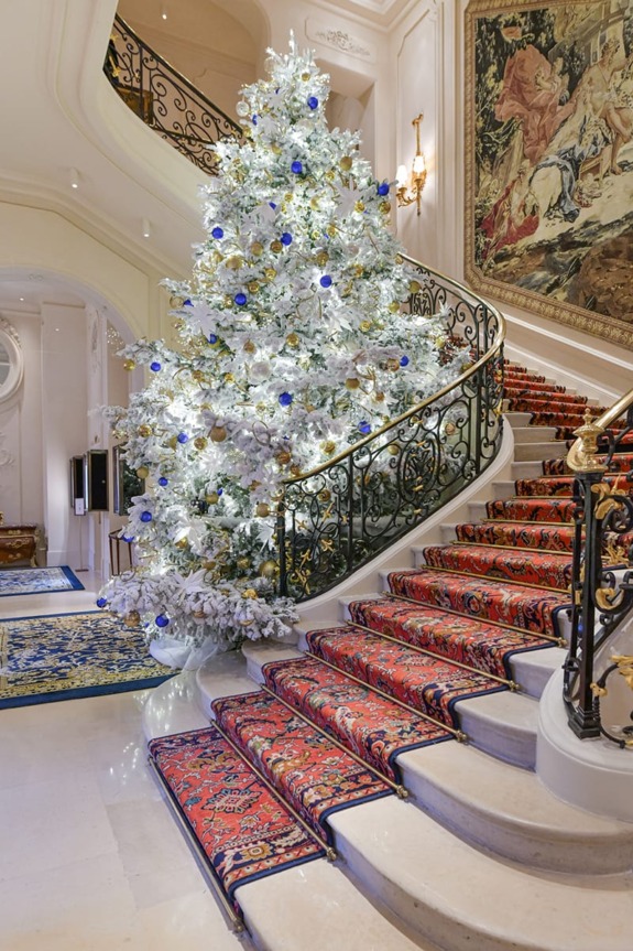 Elegant spiral staircase with ornate railing, adorned with a large decorated Christmas tree and intricate carpet runner.