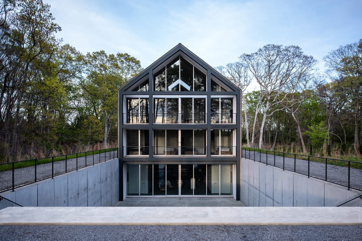 Modern glass and concrete house with a gabled roof, surrounded by trees and a sunken entryway.