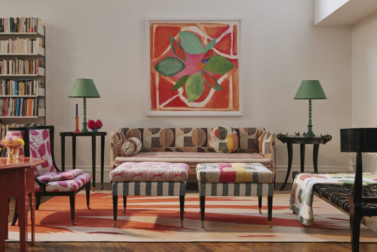 Colorful living room with patterned furniture, abstract art on the wall, green lamps and a bookshelf filled with books.
