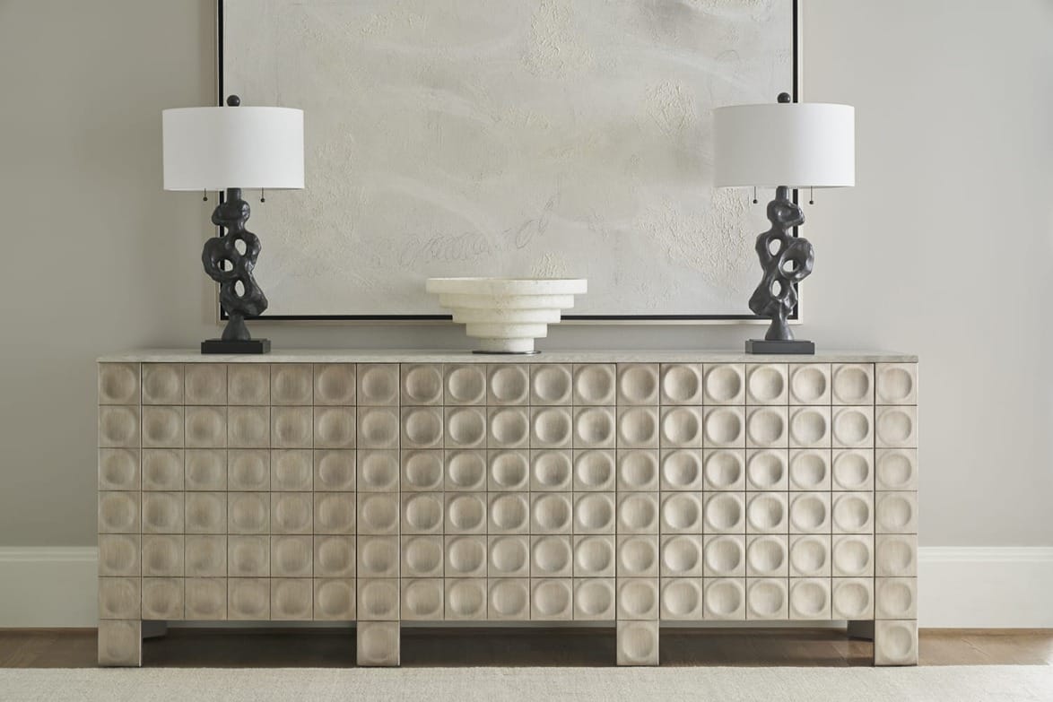 Modern sideboard with geometric patterns, topped with two artistic lamps and a decorative white bowl, against an abstract painting.