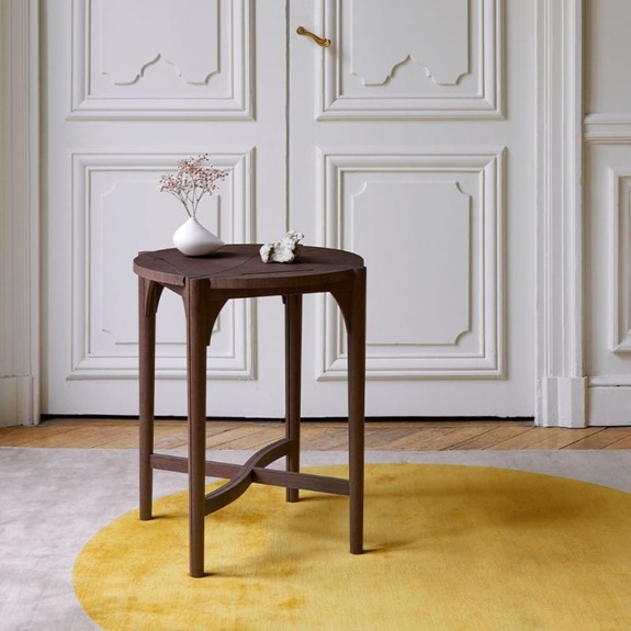 Elegant wooden side table with small white vase placed in a spacious room with white panel doors and a yellow round rug.