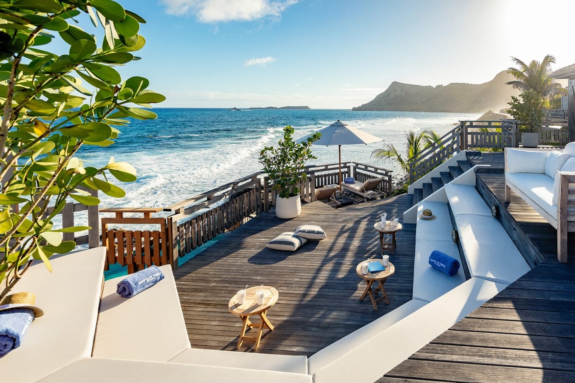 Oceanfront wooden deck with lounge seating, umbrella, and scenic view of coastline under a clear blue sky.