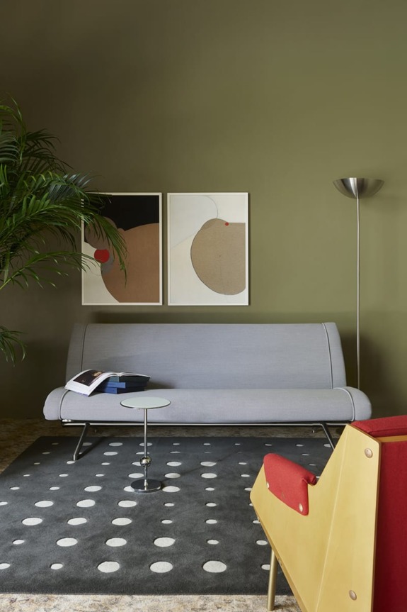 Modern living room with gray sofa, geometric art, polka dot rug, and a plant next to a floor lamp.