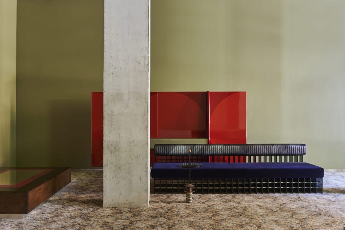 Modern minimalist living room with green walls, a red coffee table, blue sofa, and large concrete column.