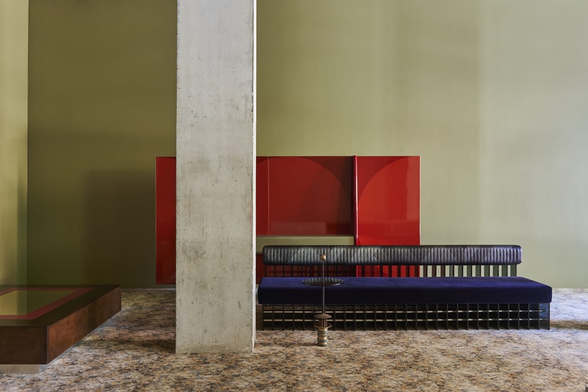 Modern minimalist living room with green walls, a red coffee table, blue sofa, and large concrete column.