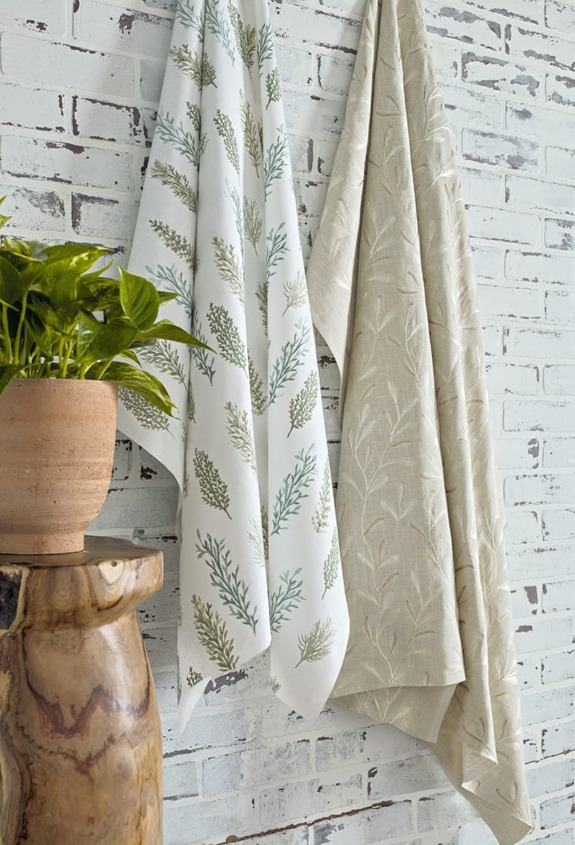 Two patterned towels hanging on a white brick wall next to a wooden table with a potted plant.