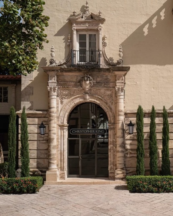 Elegant building facade with ornate stone archway, potted plants, and a sign reading "Christopher King" above the entrance.