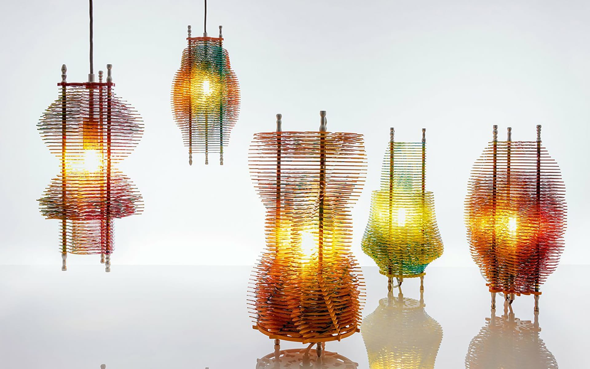 Colorful stacked glass lamps in various shapes illuminated on a glossy surface against a plain white background.