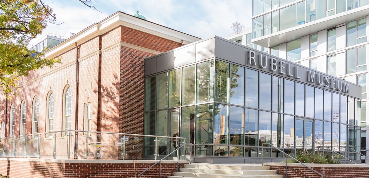 Modern glass entrance of Rubell Museum alongside red brick building under a clear sky.