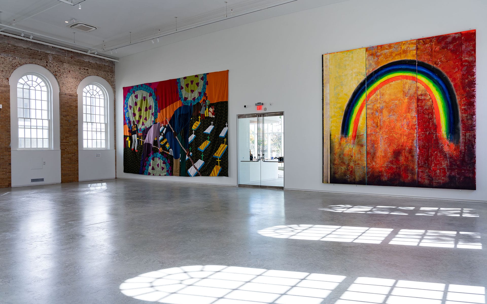 Art gallery interior with two large colorful paintings on the walls, arched windows letting in natural light.
