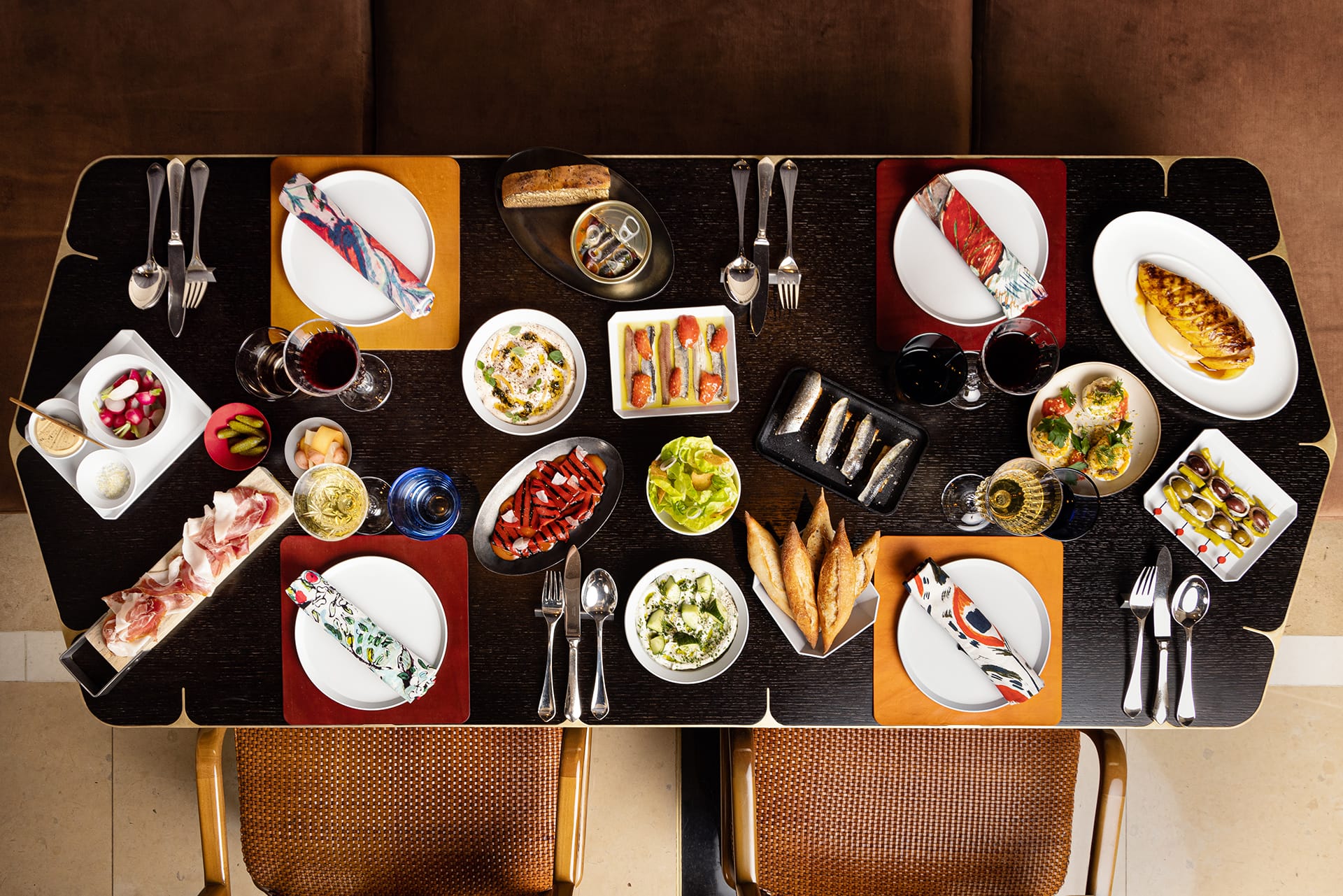Aerial view of a dining table set with a variety of colorful dishes, appetizers, and drinks for a meal.