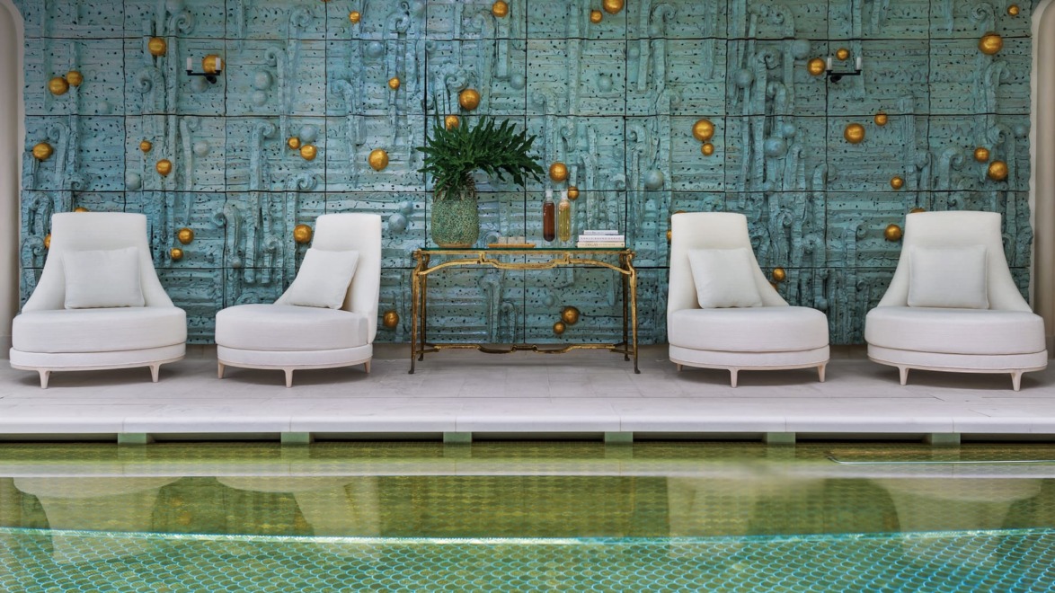 Luxurious poolside seating area with white chairs and a decorative teal and gold wall backdrop.