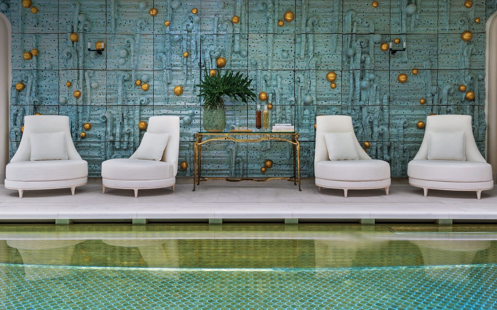 Luxurious poolside seating area with white chairs and a decorative teal and gold wall backdrop.