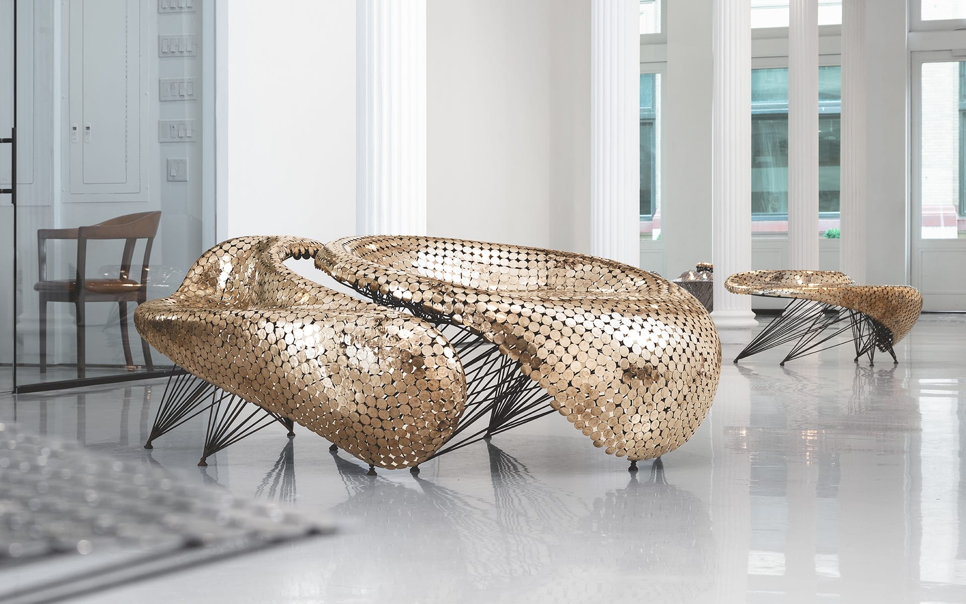 Futuristic gold seating with intricate metallic design in a modern lobby with large windows and white pillars.