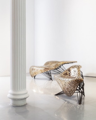 Modern art chairs with woven design next to a white column in a minimalistic gallery setting.