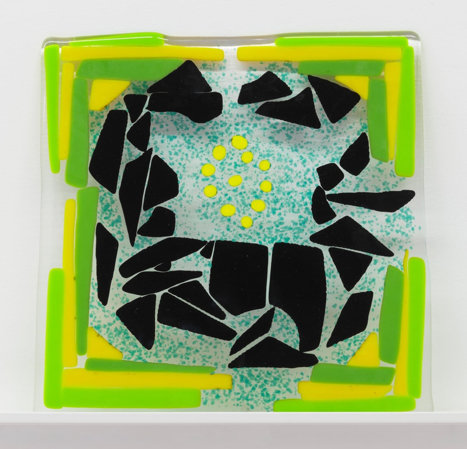 Colorful abstract glass mosaic with black, green, and yellow shapes arranged in a dynamic pattern on a speckled background.