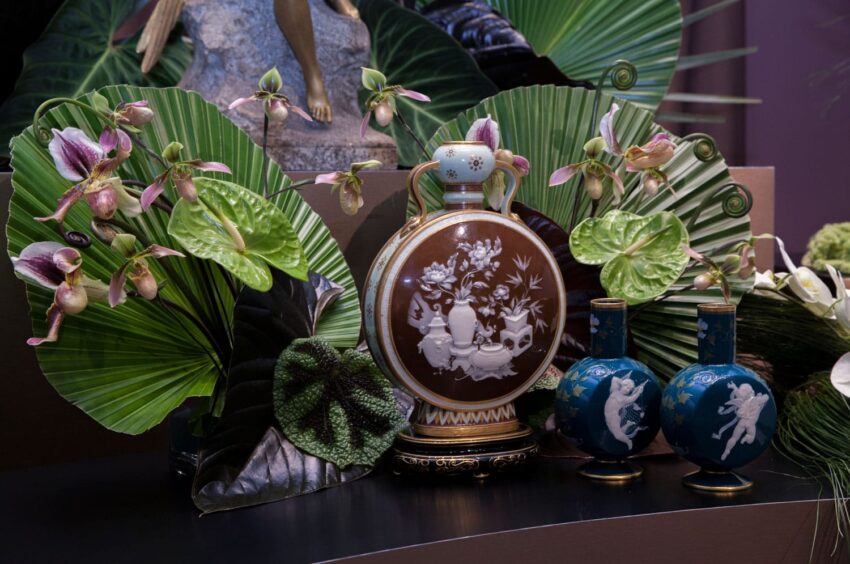 Ornate vases with intricate designs surrounded by lush green leaves and delicate pink and white flowers.