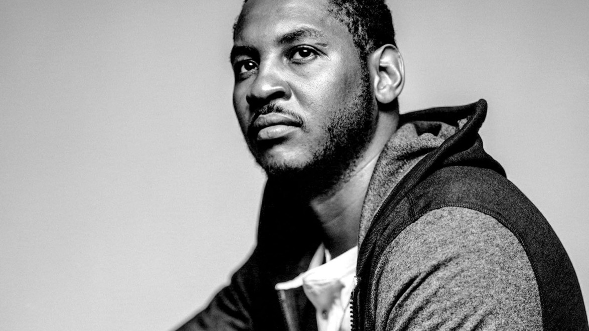 Man wearing a hoodie, looking up with a thoughtful expression in a black and white portrait.