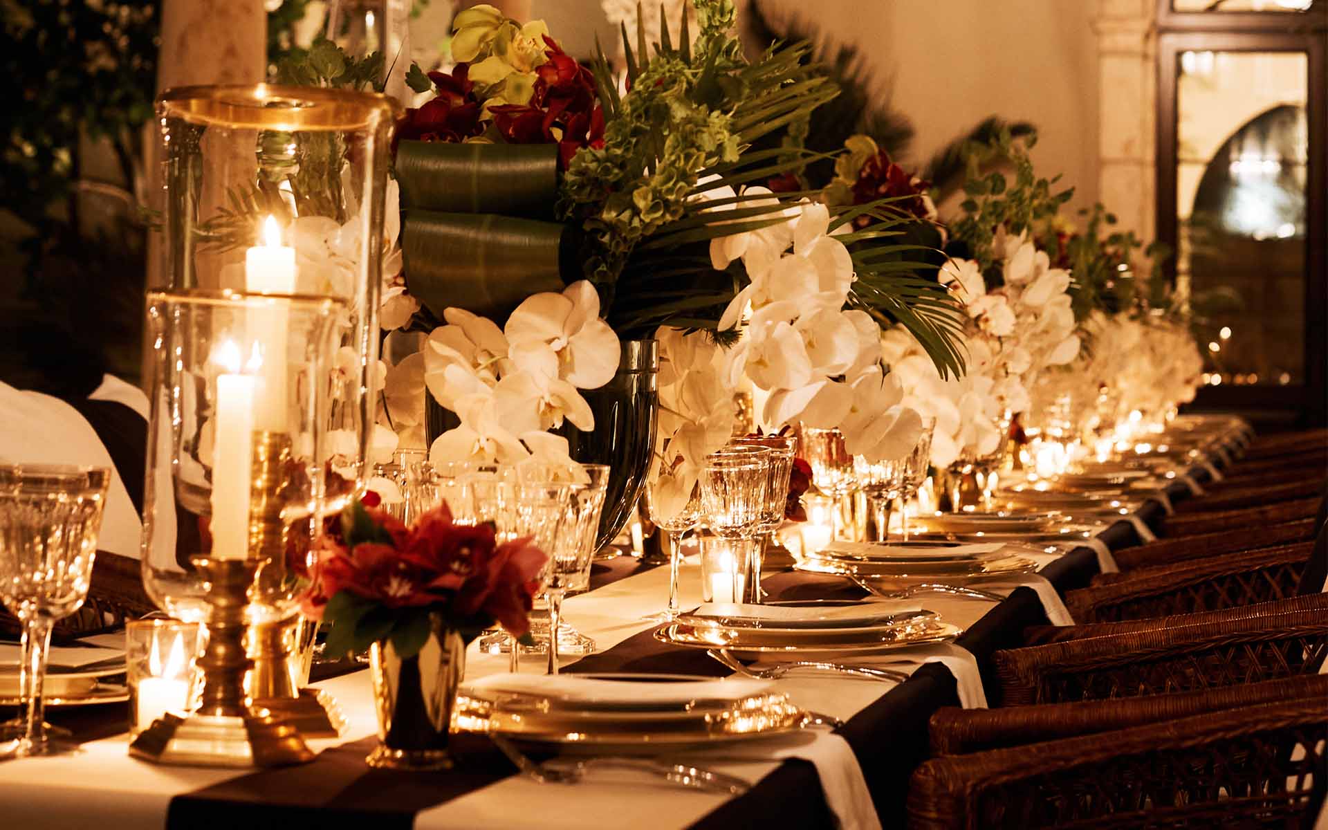 Elegant dinner table setting with candles, orchids, and greenery creating a warm, inviting ambiance for a special event.