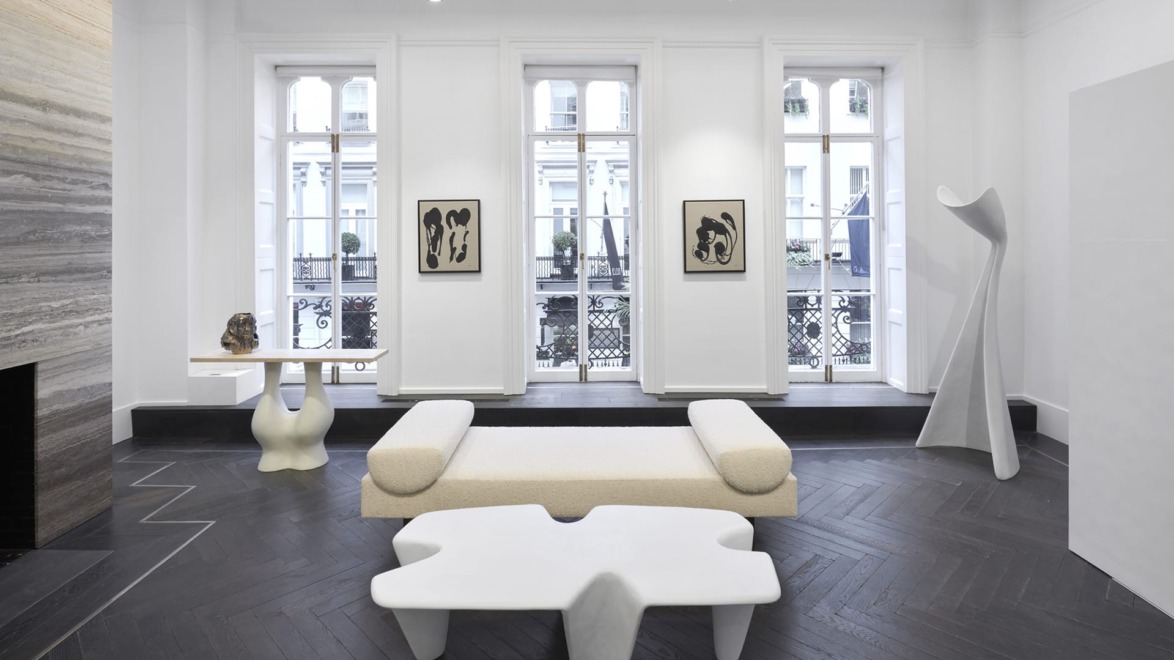 Modern minimalist living room with sculptural furniture, large windows, and abstract art on the walls.
