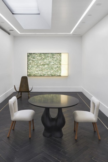 Modern room with round black table, two white chairs, abstract art on wall, and dark wooden floor.