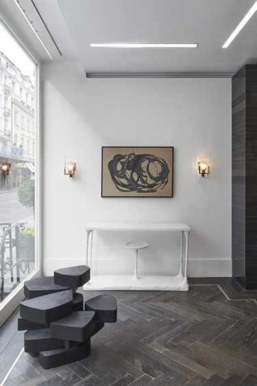 Modern art gallery interior with abstract painting, geometric sculpture, and large window overlooking a city street.