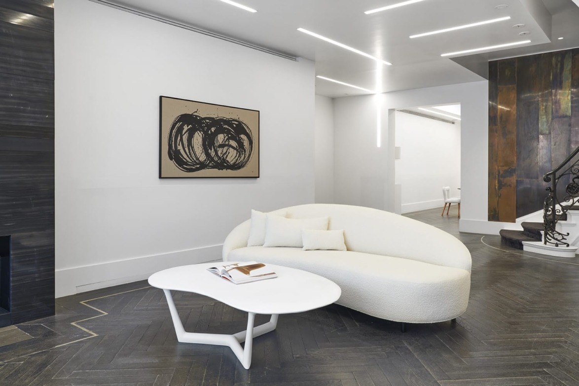 Modern living room with a curved white sofa, abstract wall art, and a white coffee table on dark wood flooring.