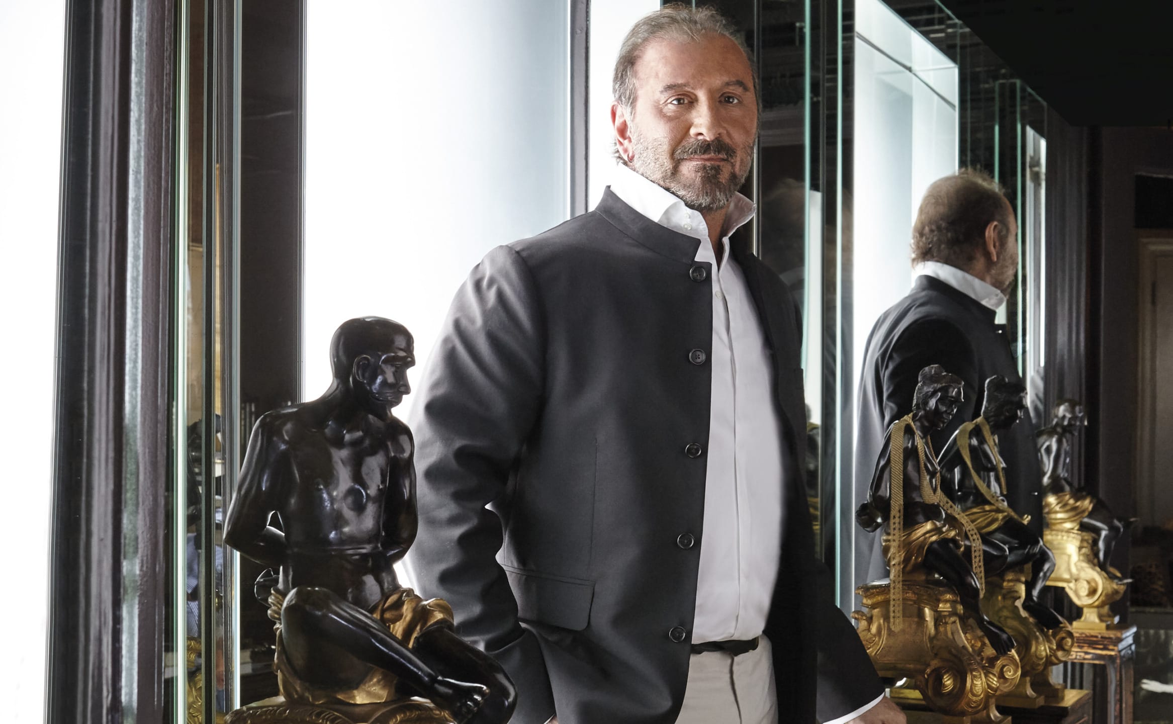 Man in a black jacket standing next to decorative statues in a mirrored room.