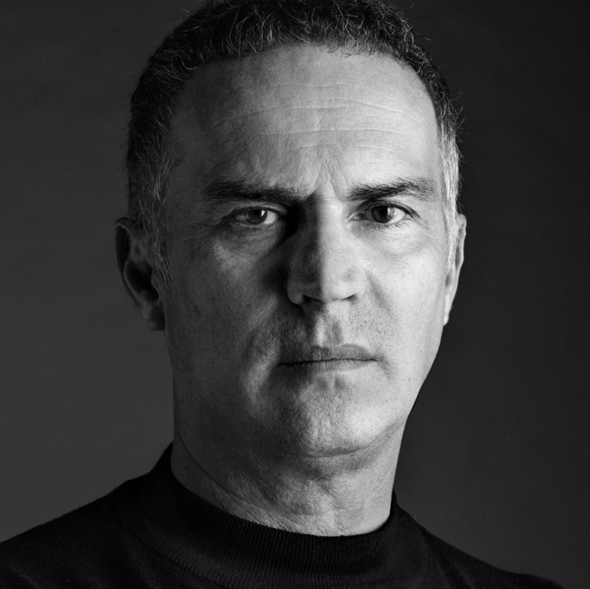 Black and white portrait of a mature man with a neutral expression, wearing a dark shirt, looking directly at the camera