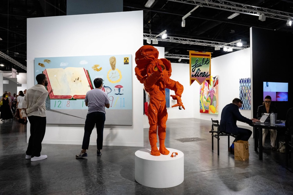 Art exhibition with visitors viewing paintings and a red astronaut sculpture on display in a modern gallery setting.