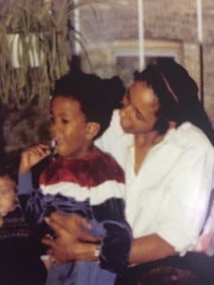 Adult holding a young child blowing bubbles indoors, with blurred background and a plant.