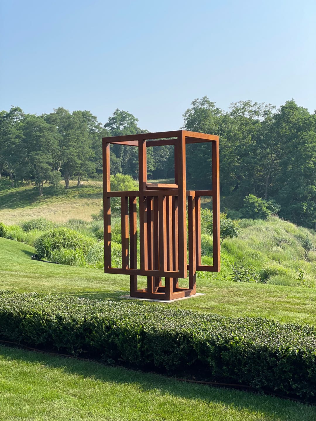 Abstract outdoor sculpture on a grassy lawn surrounded by lush greenery and trees in the background.