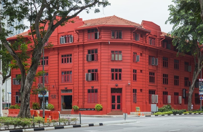 Bright red colonial-style building on a corner street with trees, showcasing vibrant architecture amidst an urban setting.
