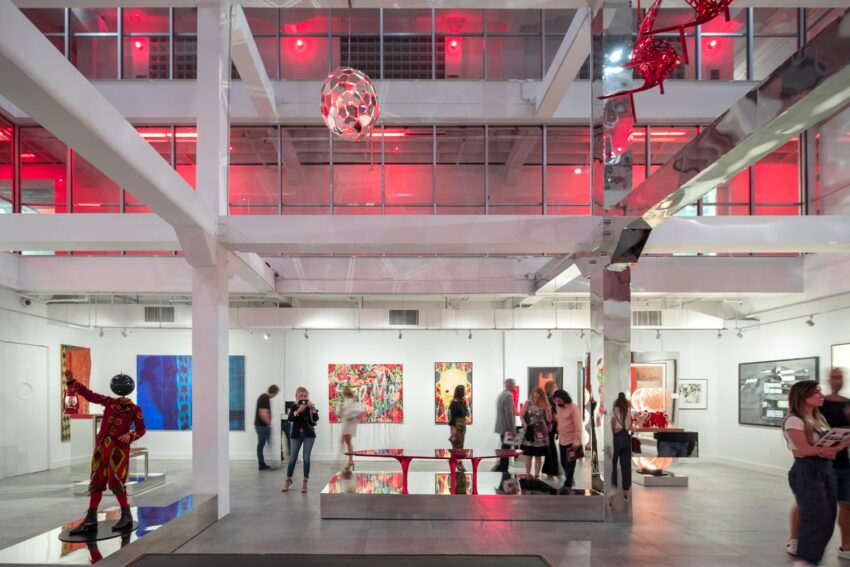 Art gallery with modern installations, people viewing colorful artworks, red lighting highlighting the contemporary space
