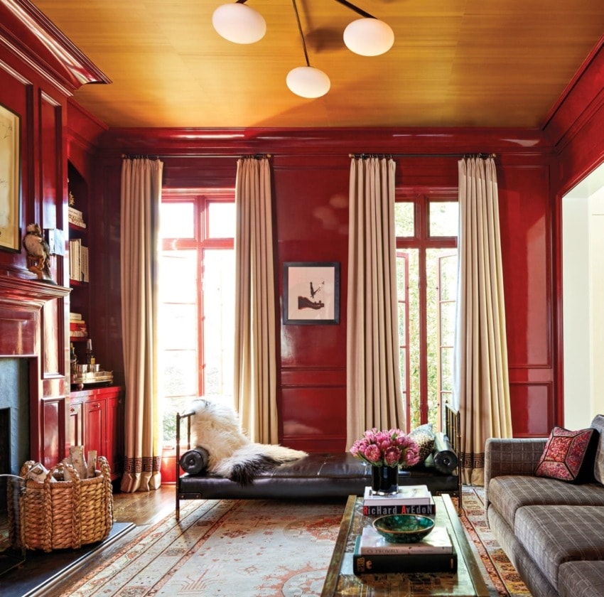 Elegant living room with red walls, tall curtains, a plush chaise, modern lighting, and decorative accents creating a cozy ambiance.