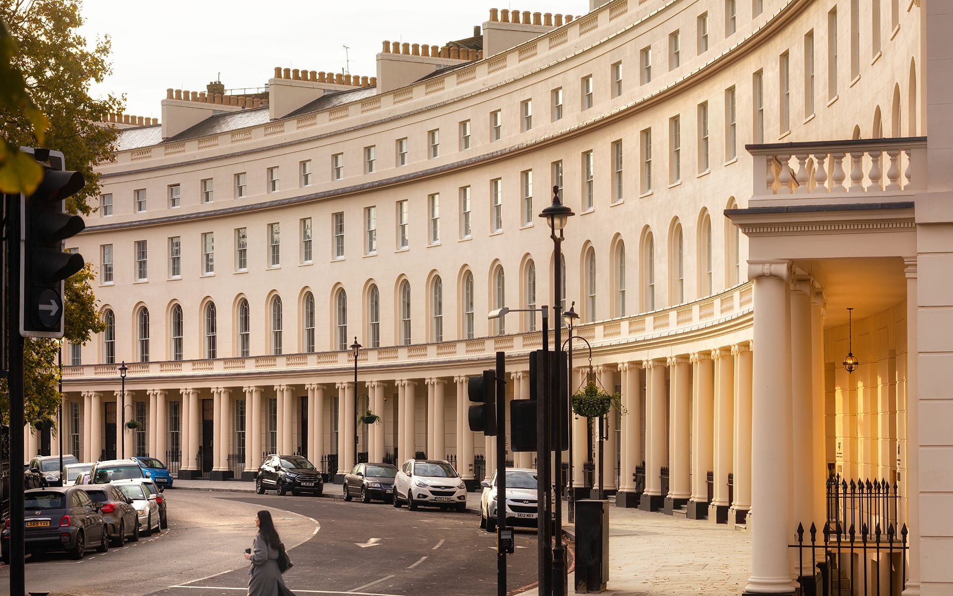 Curved row of elegant white buildings with cars parked along the street in an urban setting.