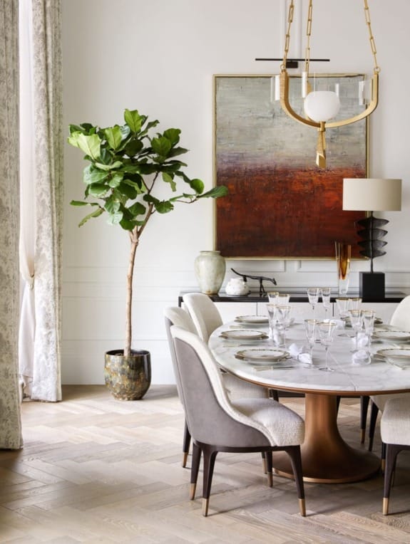 Elegant dining room with marble table, gray chairs, potted plant, modern chandelier, and abstract painting on wall.