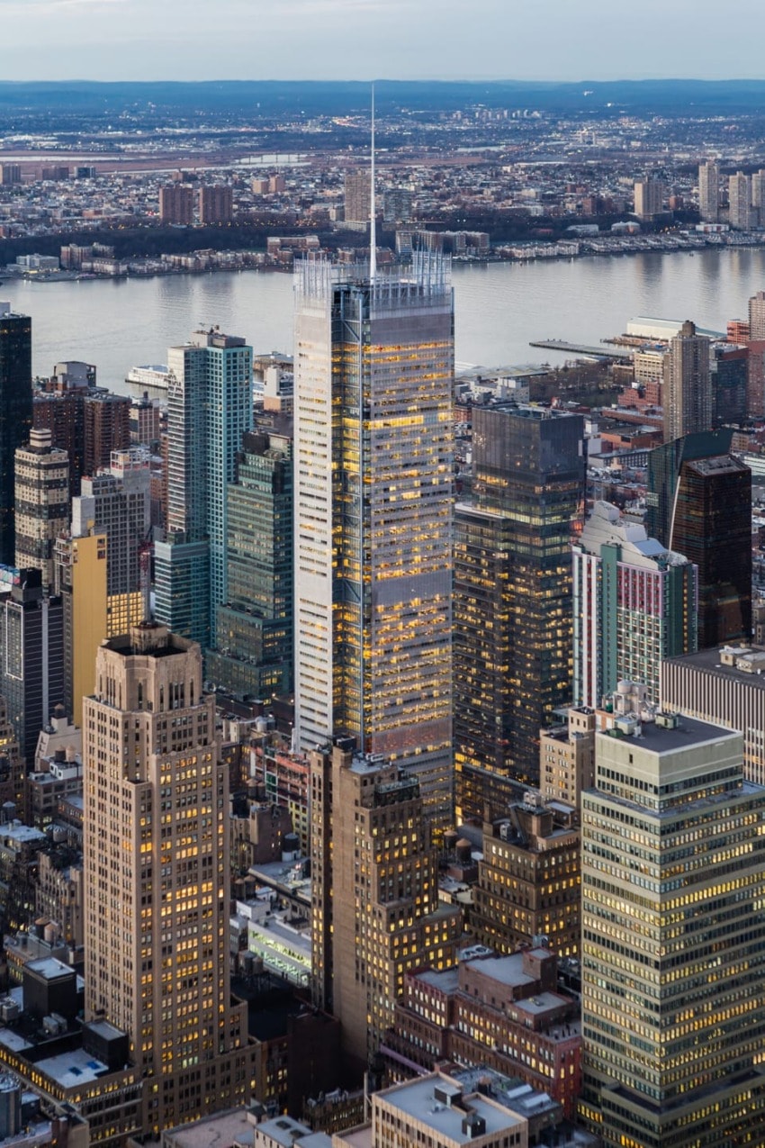 Aerial view of city skyline with tall skyscrapers, river in the background, and densely packed buildings in the foreground.