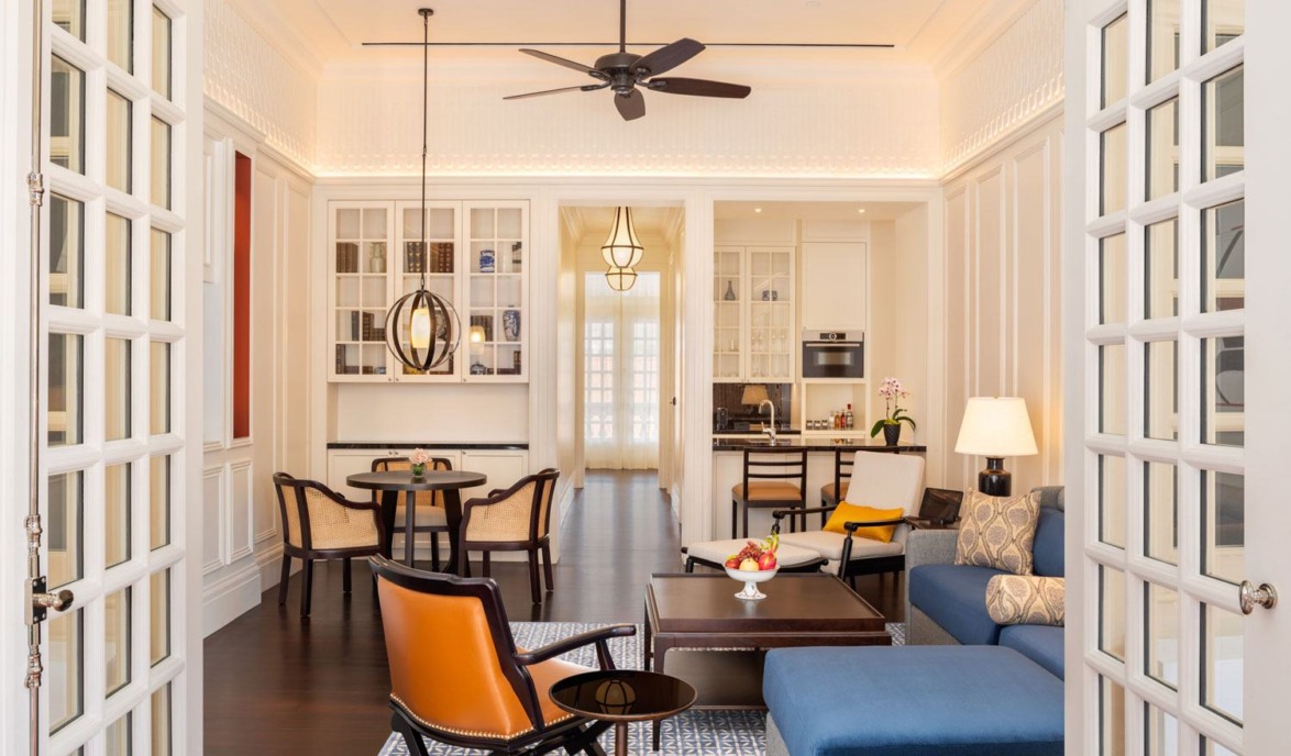 Elegant living room with modern decor, featuring orange chairs, blue sofa, wooden furniture, and a ceiling fan.
