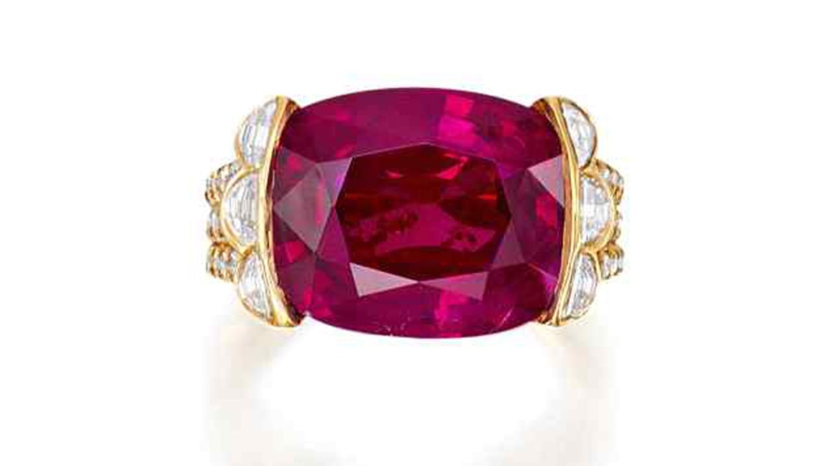 Large red gemstone set in a gold ring with diamond accents on the sides.