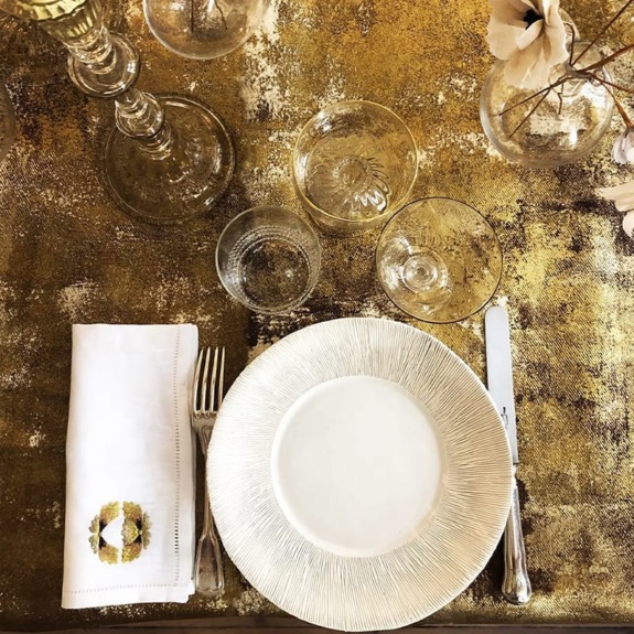 Elegant dining setup with a white plate, glasses, cutlery, and a decorated napkin on a gold textured tablecloth.