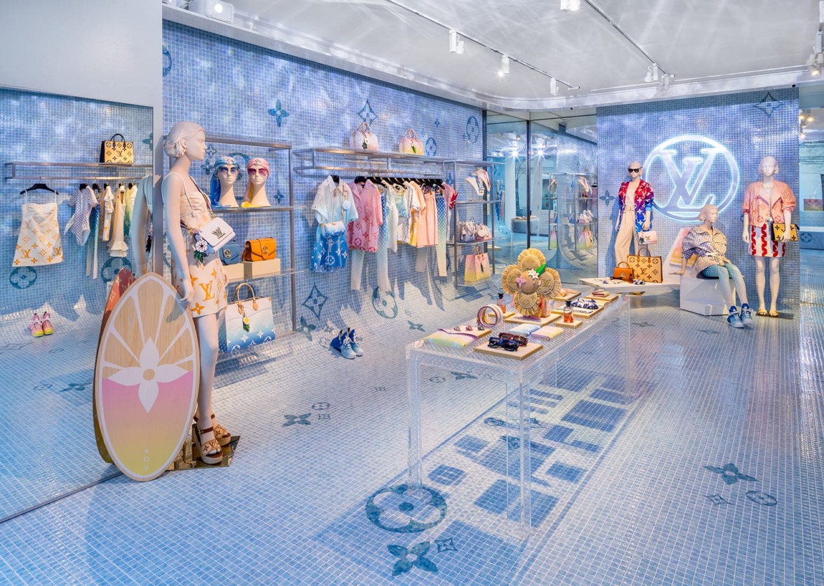 High-end fashion store interior with colorful clothes, accessories, and stylish mannequins on a blue patterned floor and walls.