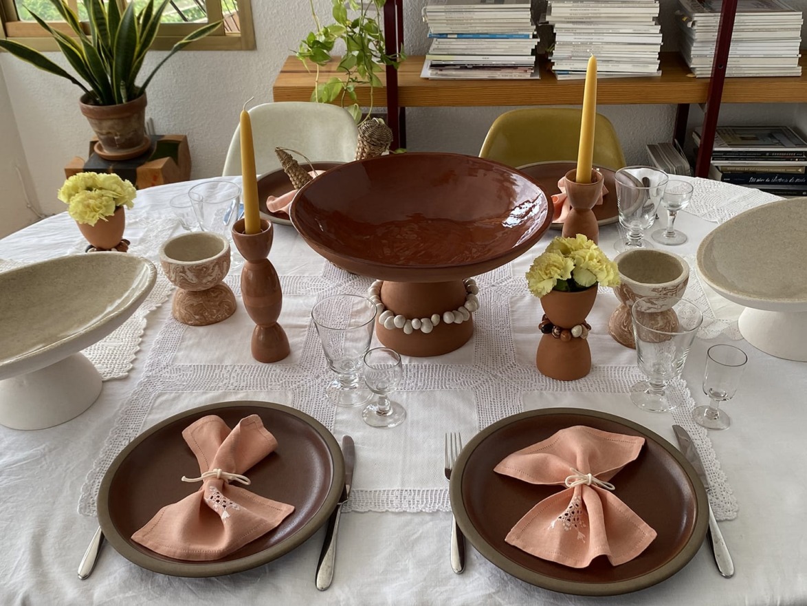 Elegant table setting with ceramic plates, peach napkins, candles, and flowers on a white tablecloth.