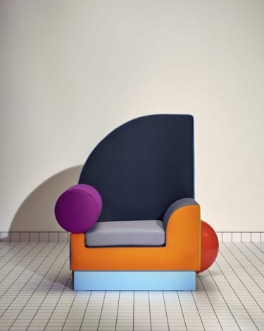 Colorful modern chair with geometric shapes and a unique design on a tiled floor against a neutral background.