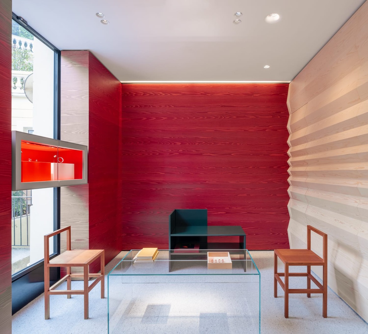 Modern interior with wooden chairs, glass table, vibrant red accent wall, and large window displaying a street view.