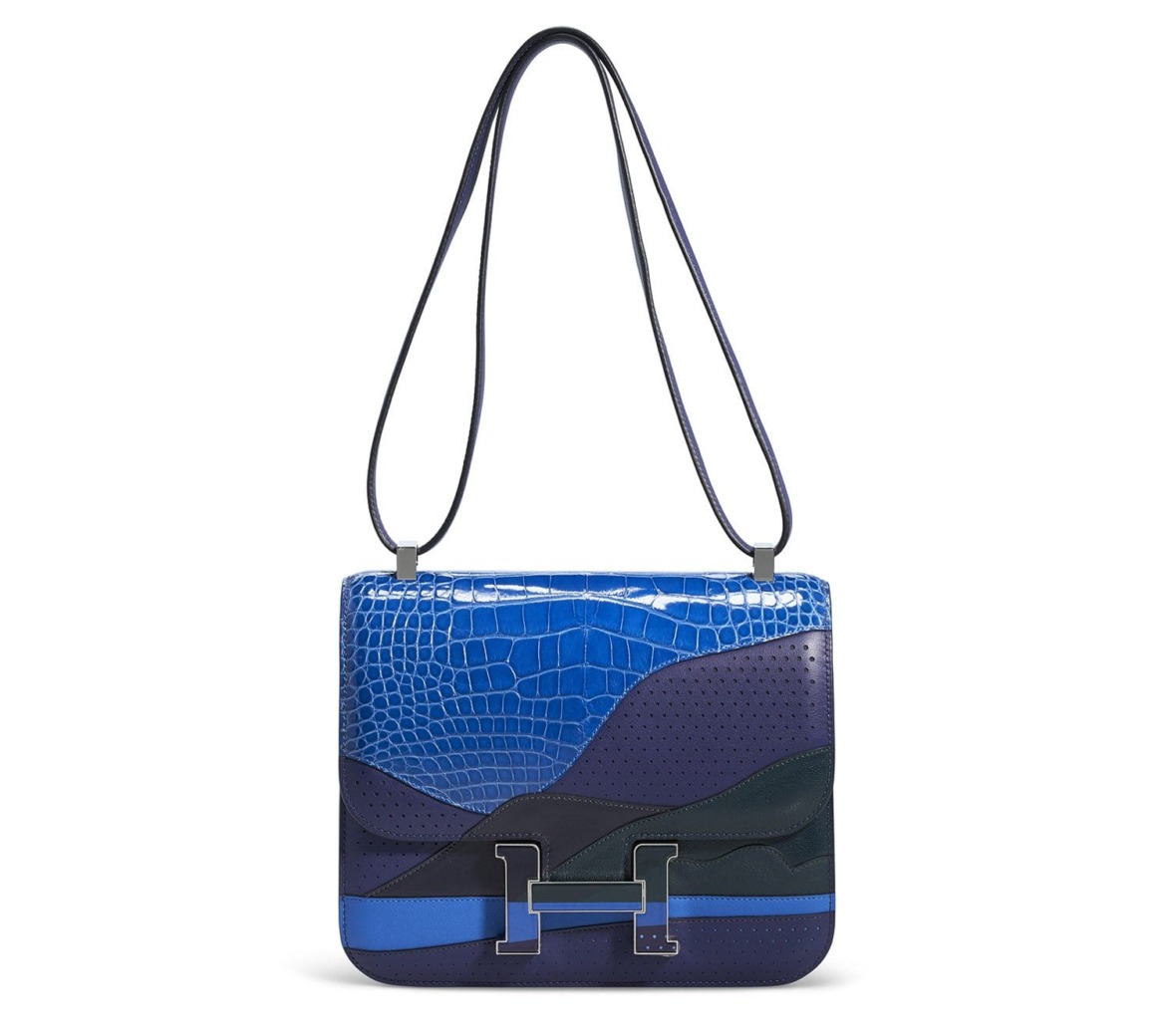 Blue handbag with abstract design and textured pattern, featuring a long strap and metallic clasp.