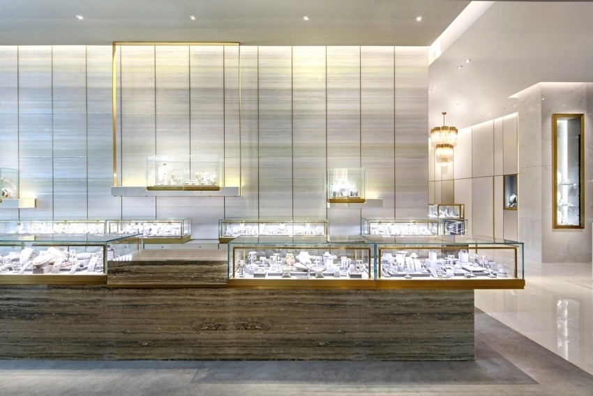 Luxury jewelry store interior with gold-accented display cases showcasing various jewelry pieces under bright lighting.