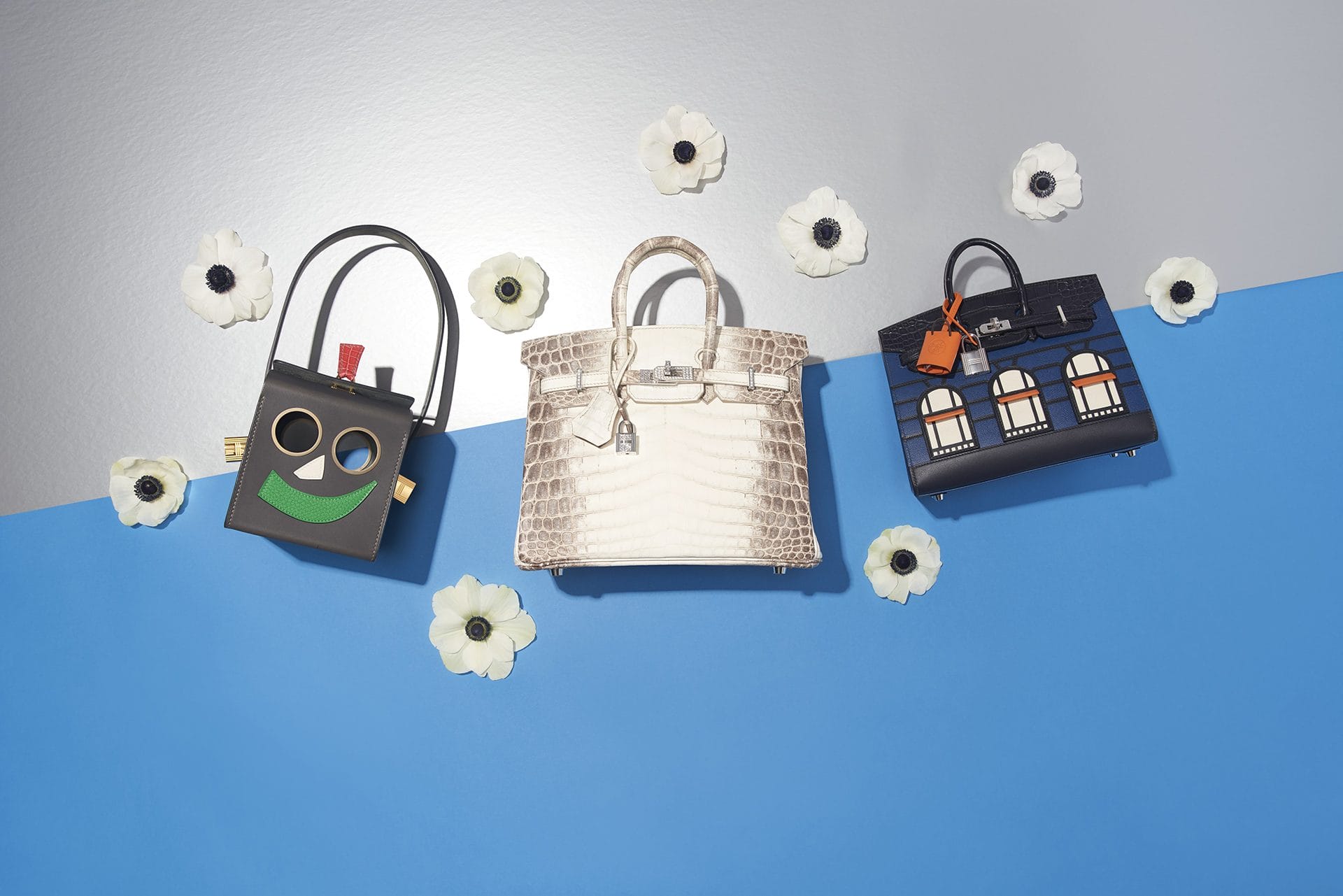 Three designer handbags on a blue and gray background surrounded by white flowers.